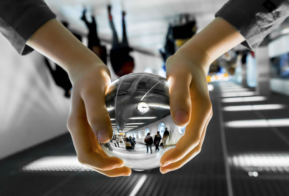 Image of airport walkway reflected in glass ball held by person