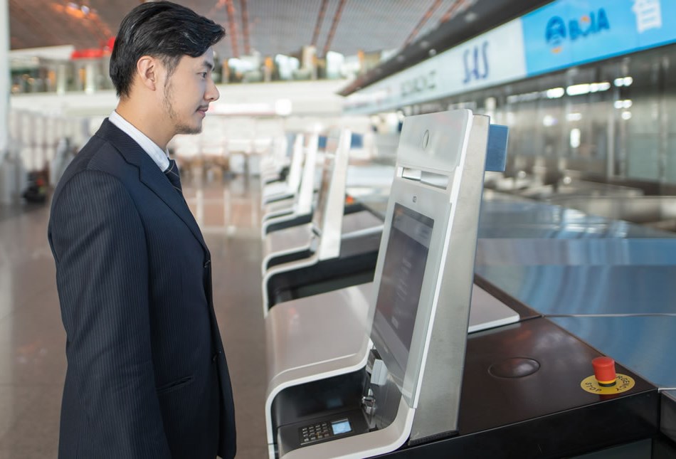 Provide a low-touch airport experience Person standing at self bag-drop kiosk in airport